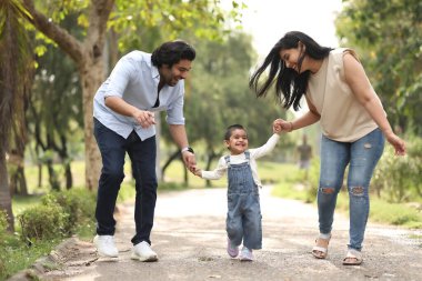 Ebeveynler mutlu bir şekilde gülen çocuklarına yeşillik dolu yemyeşil bir parkta rehberlik ederler..