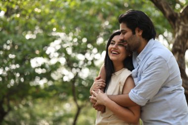 Bir çift, yeşilliklerle çevrili güneşli bir parkta kahkaha ve şefkat paylaşıyor..
