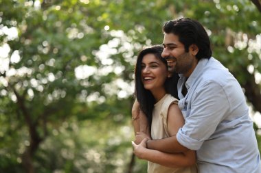 Erkek ve kadın neşeli bir öğleden sonra güneşli bir parkta kucaklaşırken neşeyle gülüyorlar..
