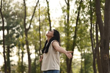 Bir kadın gür bir ormanda duruyor, kollarını açmış, etrafındaki temiz hava ve sükuneti kucaklıyor..