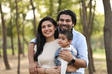 Gündüz vakti küçük çocuklarını yeşil bir parkta tutarken sıcak bir şekilde gülümseyen bir çift..