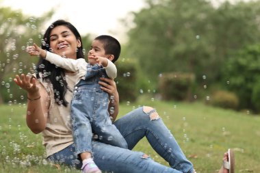 Bir anne ve çocuğunun güneşli bir park ortamında kabarcıklarla oynadığı neşeli bir an..