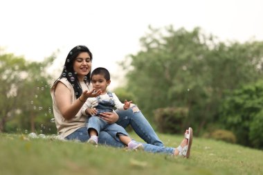 Neşeli bir anne ve küçük oğlu, güneşli bir günde parkta kabarcıklarla oynuyorlar..