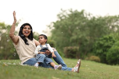 Neşeli bir anne ve çocuğu güneşli bir günde çimenlikte kabarcıklarla oynuyorlar..