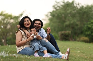 Aile çimenlerin üzerinde rahatlar, güler ve çocuklarıyla oynarlar, güneşli bir günün tadını çıkarırlar..