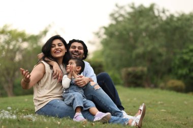 Aile çimenlerde dinlenir, gülümser ve oynar, güneşli bir öğleden sonra neşeli bir atmosferle..