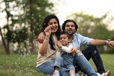 Neşeli bir aile, güneşli bir öğleden sonra yeşil bir parkta köpüklerle oynayıp güzel anılar yaratıyor..