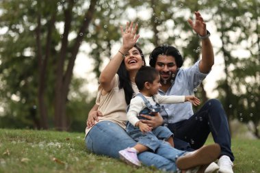 Neşeli bir aile çimenlerde rahatlar, kabarcıklarla oynar ve doğada birlikte kaliteli vakit geçirmenin tadını çıkarır..