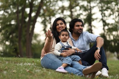 Üç kişilik bir aile, parkta kabarcıklarla oynarken güneşli bir günün tadını çıkarıyor..