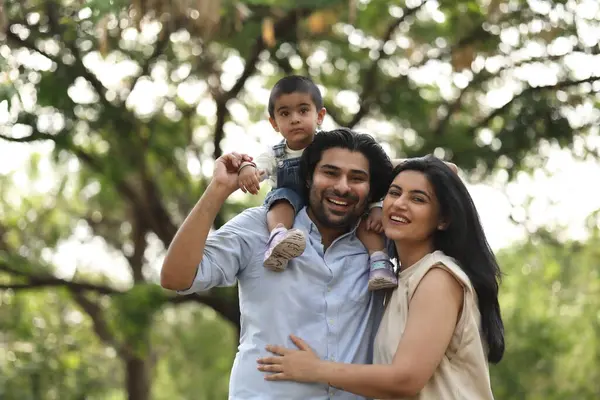 Bir aile, yeşil bir parkta, çocuklarıyla oynarken gülümseyerek ve gülerek kaliteli vakit geçirmekten zevk alır..