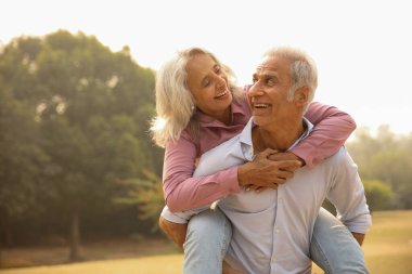 Zinde bir çift, güneşli bir parkta, sevgi ve mutluluğu sergileyerek sırtına binerken aynı kahkahayı paylaşır..
