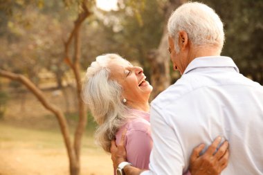 Yaşlı Asyalı çift gün batımında doğa ve ağaçlarla çevrili bir parkta dans ederken kahkaha ve aşkı paylaşıyor..