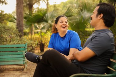 Hintli romantik çift bir bankta otururken konuşuyor ve gülüyor. Huzur parkında birlikte vakit geçiriyorlar..