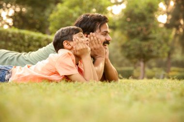 Mutlu baba oğul yan bakışı Parktaki çimlerde yatar ve dümdüz karşıya bakar.