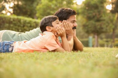 Bir baba ve oğulun otların üzerinde yüzüstü uzanmış, çenelerini ellerinin üzerinde dinlendirirken çekilmiş fotoğrafları..