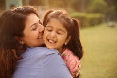 Parkta kucaklaşan bir anne ve kızın sıcak, sevgi dolu bir bağı paylaşması..