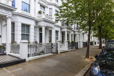 A peaceful Notting Hill street with white terraced houses and green trees lining the road clipart