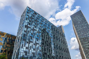 Londra 'da çarpıcı bir cam bina yansıtıcı cepheler, gösterişli şehir mimarisi ve canlı mavi bir gökyüzü arkaplanı içeriyor.