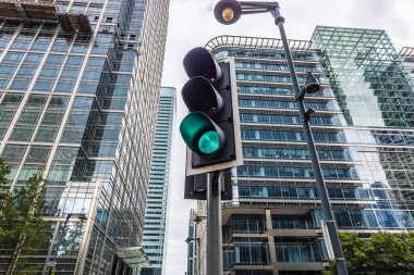 Green traffic light with modern skyscrapers in the background, showcasing urban design and city architecture clipart