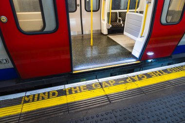 İstasyonda açık kapıları olan bir Londra metro treni, ikonik - Boşluğa dikkat - uyarısı