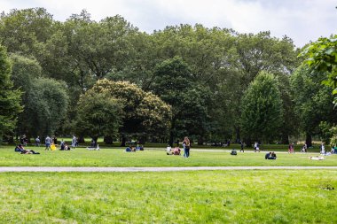 Güneşli bir günde dinlenen, yürüyen ve doğanın tadını çıkaran insanların olduğu güzel yeşil bir park.