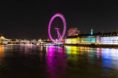 Londra Gözü 'nün göz kamaştırıcı görüntüsü gece canlı renklerde parlıyor. Huzurlu Thames yansımalarıyla tamamlanıyor.