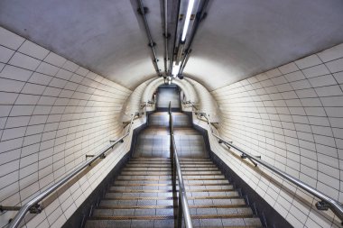 Simetrik metro merdiveni fayanslı duvarlar, aydınlatılmış kemer yolu ve modern ulaşım altyapısı.