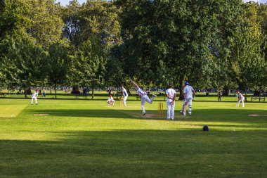 Parktaki amatör kriket oyunu. Beyazlı oyuncular güneşli bir zemine karşı.