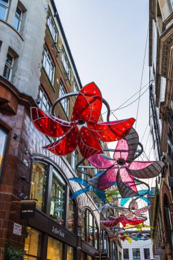 Binaların arasında asılı büyük kırmızı ve pembe çiçekli çarpıcı sokak süslemeleri şehre şenlik havası katıyor. Londra, İngiltere, 2 Eylül 2023