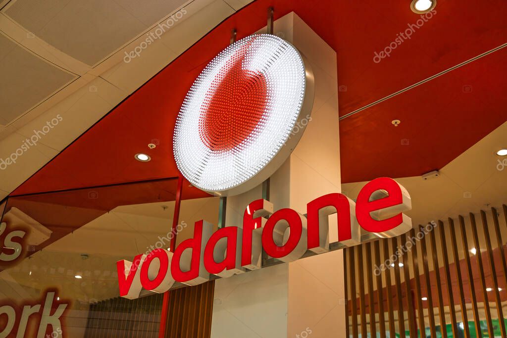 Vodafone store in a shopping mall with a large illuminated logo and bold red branding. London, UK, 28 October 2023