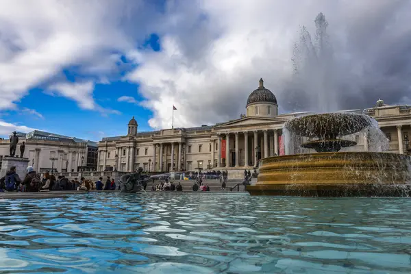 Trafalgar Meydanı ikonik çeşmesi ve bulutlu mavi gökyüzünün altında Ulusal Galeri