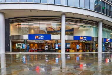 Şehir Metro Bankası şubesi çağdaş bir tasarım, dijital ekranlar ve yağmurlu asfalt yansımalarını sergiliyor. Londra, İngiltere, 10 Aralık 2023