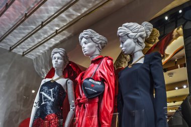 Moschino 'nun yüksek moda elbiseleri bir butik vitrindeki mankenlerin üzerinde sergileniyor ve koyu kırmızı ve siyah renkte gösteriliyor. Londra, İngiltere, 17 Aralık 2023