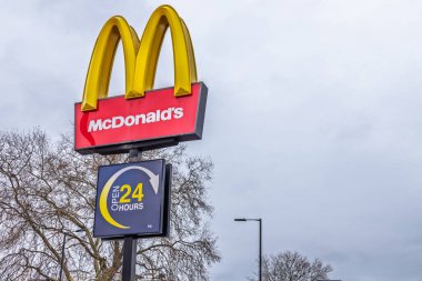 McDonald 24 saat işareti, bulutlu bir gökyüzünde altın kemerlerle duruyor. Londra, İngiltere, 25 Aralık 2023