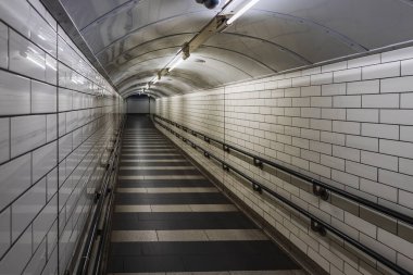 Londra metrosunda boş fayanslı tünel, floresan ışıkları ve perspektif çizgileri var..