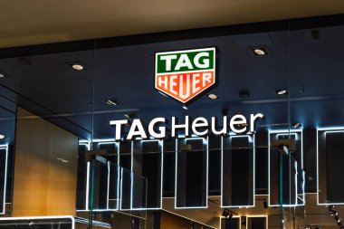 TAG Heuer, lüks bir alışveriş merkezinde ışıklı tabelalı ve simgesel logolu bir butik girişi izle. Londra, İngiltere, 10 Şubat 2024