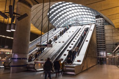 Canary Wharf Jubilee Line istasyonunun içinde yürüyen merdivenler, modern mimari ve Londra metro istasyonunda gezen banliyö görevlileri var. Londra, İngiltere, 17 Şubat 2024