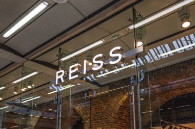 Reiss mağazasının dış cephesinde lüks bir alışveriş merkezindeki cam üzerine aydınlatılmış logo var. Londra, İngiltere, 25 Şubat 2024