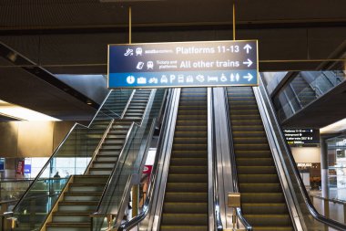 Modern tren istasyonu içinde yürüyen merdivenler ve yukarıdaki ışıklı yön işaretleri var. Londra, İngiltere, 25 Şubat 2024