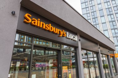 Sainsbury Yerel Mağazası girişi. Çağdaş bir şehir ortamında ışıklı tabela ve cam mağaza önü var. Londra, İngiltere, 3 Mart 2024