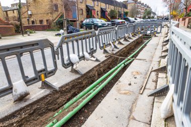 Şehir sokak inşaatı, açık siperleri koruyan metal bariyerler ve yeşil borular. Londra, İngiltere, 3 Mart 2024