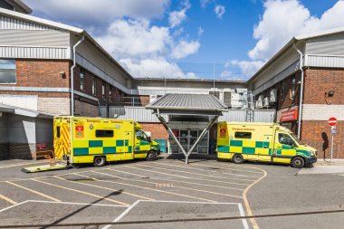 Güneşli bir günde modern bir ambulans istasyonunun önüne park edilmiş iki sarı ambulans. Londra, İngiltere, 24 Mart 2024