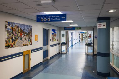 Hastane koridorunda modern bir sağlık ortamında yön tabelaları, çizimler ve temiz mavi döşemeler var. Londra, İngiltere, 24 Mart 2024