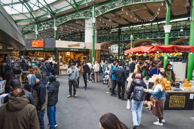 Canlı Borough Market 'in içi renkli gıda tezgahlarına ve satıcılarına göz atan müşterilerle dolu. Londra, İngiltere, 29 Mart 2024