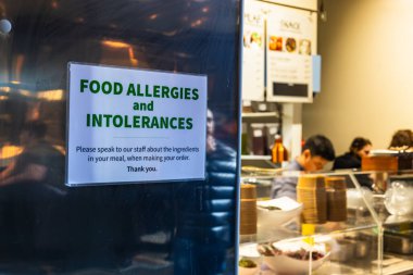 Yemek alerjisi ve hoşgörüsüzlük uyarısı bir restoranın mutfak penceresinde güvenli yemek deneyimi sağlamak için asılıdır..