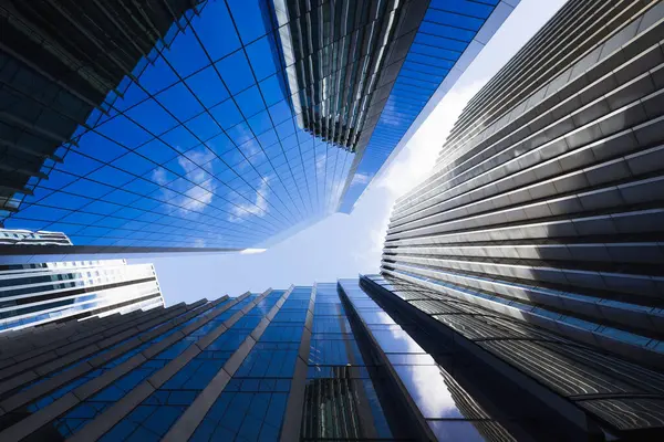 Yüksek cam gökdelenlerin yer aldığı şehir manzarası güneş ışığını ve derin mavi gökyüzünü yansıtıyor..