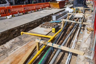 Güvenlik engelleri olan bir inşaat siperinde açıkta kalan borular ve kablolar için kentsel hizmet kurulumu çalışması.