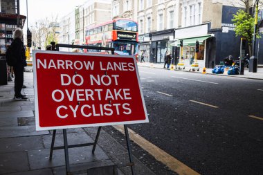 Trafik uyarı levhası, sürücülere yoğun bir caddede dikkatli olmalarını ve bisikletçileri geçmemelerini hatırlatıyor. Londra, İngiltere, 1 Nisan 2024