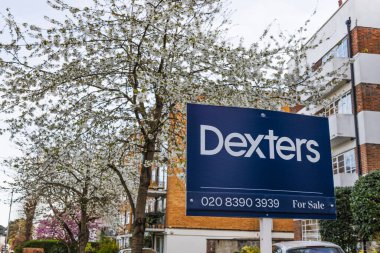 Dexter emlak ajansı yapraklı ağaçlar ve modern mimari ile şehir ortamında görünür bir tabela. Londra, İngiltere, 6 Nisan 2024