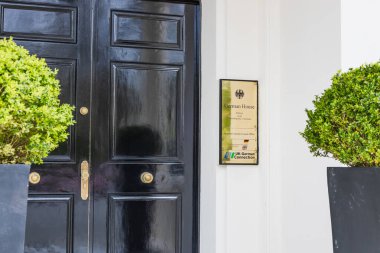 Londra, İngiltere 'deki Alman Konağı girişine yakın çekim. Resmi plaketi ve dekoratif bitkileri olan zarif siyah bir kapı. Londra, İngiltere, 6 Nisan 2024